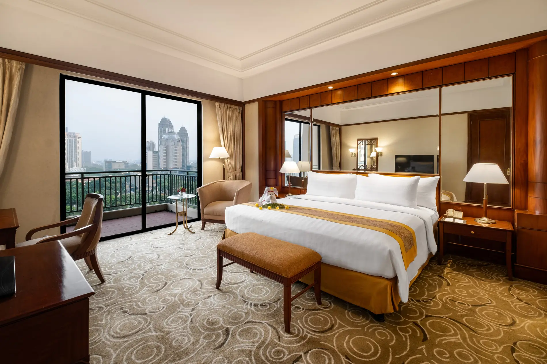 Kamar hotel sultan jakarta yang luas dilengkapi tempat tidur besar yang tertata rapi, bantal dekoratif, dan sandaran kepala yang bergaya.